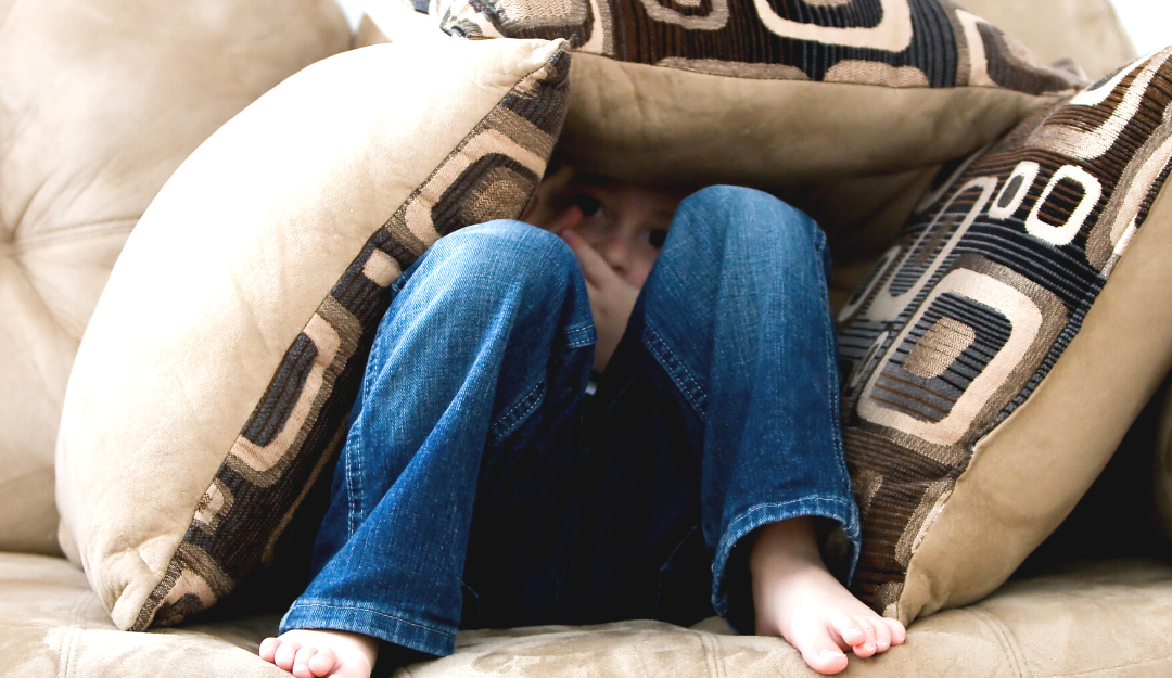 Child playing hide and seek under pillows on a couch